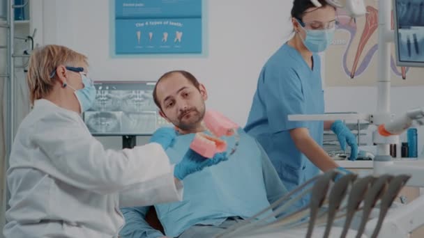 Стоматолог использует искусственную челюсть, чтобы объяснить, как правильно чистить зубы — стоковое видео