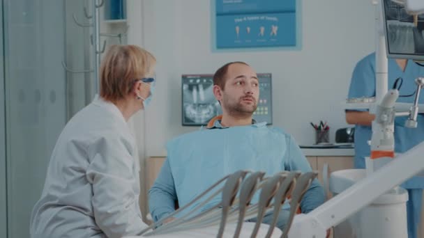 Dentista y enfermera mostrando resultados de rayos X al paciente con dolor de muelas — Vídeos de Stock