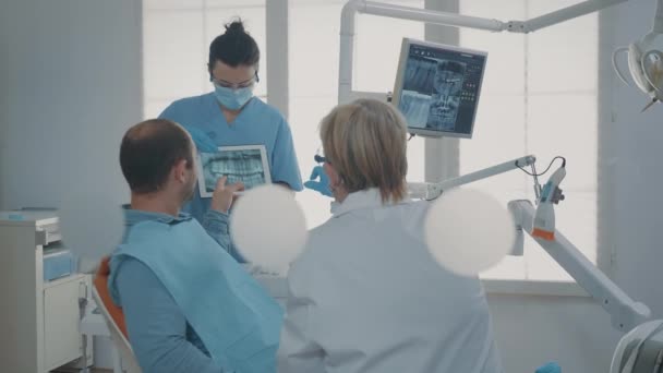 Команда стоматологов показывает рентген зубов пациенту с зубной болью — стоковое видео