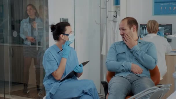 Dentistry nurse taking notes and talking to patient about toothache — Vídeo de Stock