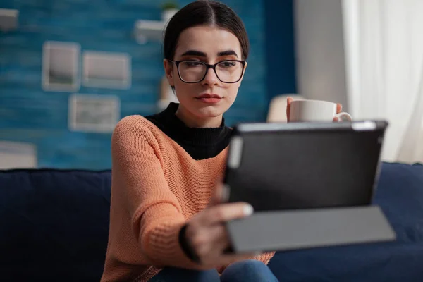 Freelancer with glasses on living room couch holding digital tablet. — Fotografia de Stock