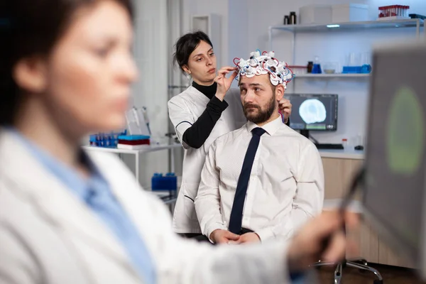 Specialist woman in neuroscience adjusting eeg headset analyzing brain activity of man — 图库照片
