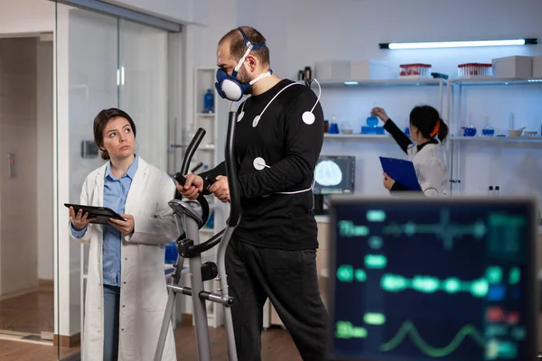 Üzerinde tıbbi elektrotlar bulunan sporcu vücut dayanıklılığında çalışan spor eğitmeniyle çalışıyor.