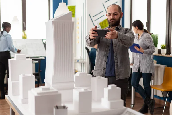 Architect working with smartphone to photograph white foam scale model — Stockfoto