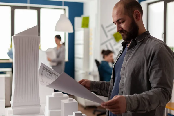 Arquitecto leyendo plano de proyecto residencial junto a maqueta de rascacielos —  Fotos de Stock