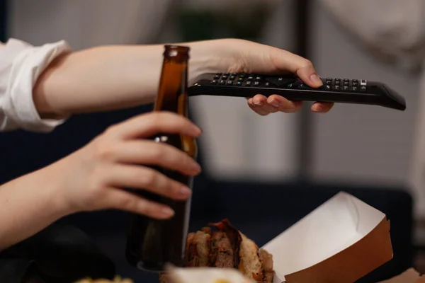 Close-up of hands holding beer bottle relaxing browsing tv channels using remote — Zdjęcie stockowe