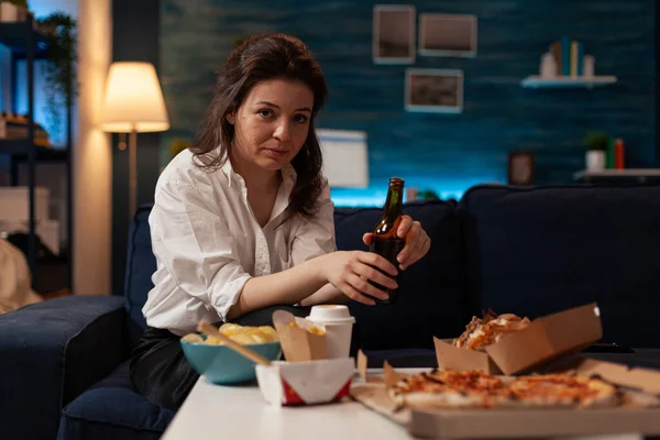 Porträt einer lächelnden Frau, die auf dem Sofa sitzend in die Kamera blickt und eine Bierflasche hält — Stockfoto