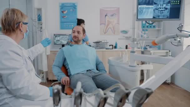 Стоматолог, який показує результати протезування зубів пацієнту під час огляду — стокове відео