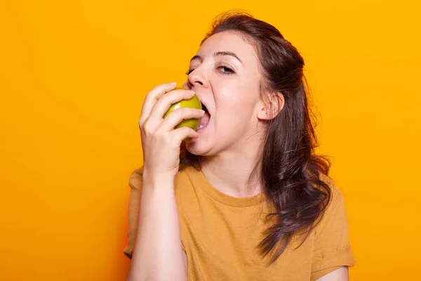 Портрет здорової жінки кусає зелене яблуко в руці на камеру — стокове фото