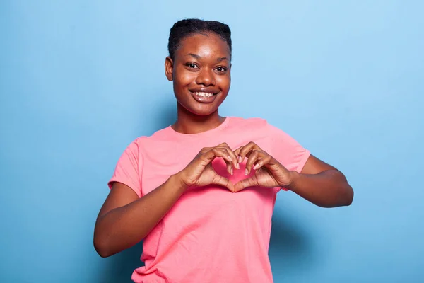 Portrait of african american young woman smiling at camera making heart shape symbol — 图库照片