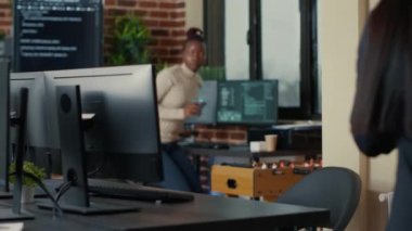 Two software developers coming at desk and sitting down holding laptop with coding interface
