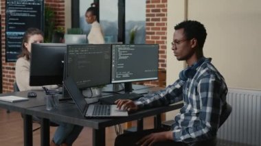 Programer thinking while touching beard and fixing glasses while typing on laptop sitting at desk