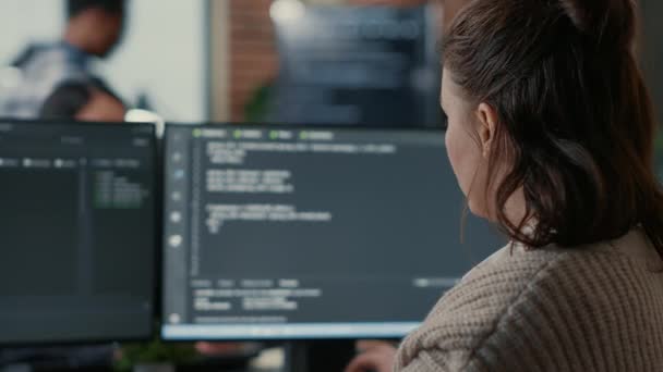 Перегляд плечей конструктора баз даних, який пише код, дивлячись на декілька екранів комп'ютера — стокове відео