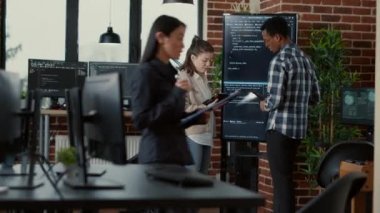Software developer holding digital tablet analyzing code on wall screen tv explaining errors to coworker programer