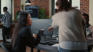 Programer pointing pencil at computer screen with software compiling code explaining source algorithm to coworker