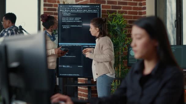 Ingénieurs système comparant le code source sur écran mural tv analyser les erreurs à l'aide d'une tablette numérique — Video