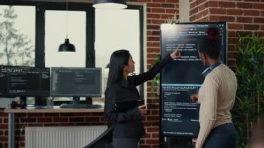 Software engineers analyzing code on wall screen tv looking for bugs and errors while colleague programer typing