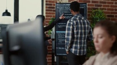 System developers analyzing code on wall screen tv looking for errors comparing results on digital tablet