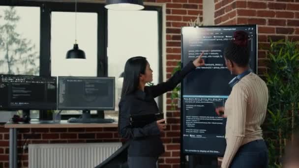 Software engineers analyzing code on wall screen tv looking for bugs and errors while colleague programer typing — Vídeo de Stock