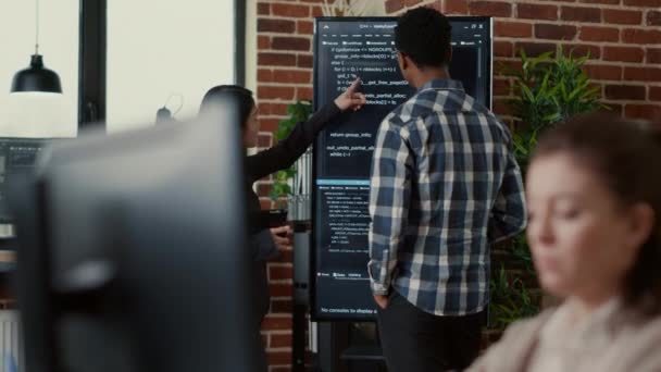 System developers analyzing code on wall screen tv looking for errors comparing results on digital tablet — Wideo stockowe