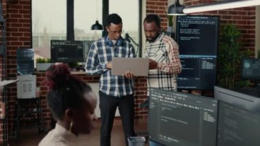 Software programmers talking about algorithms holding laptop and standing in the middle of it office