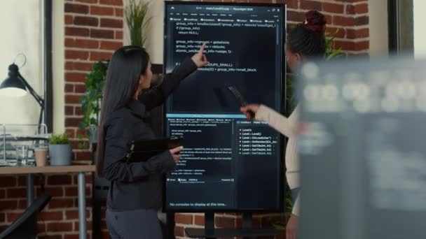 Team of programmers analyzing code on wall screen tv looking for bugs and errors — Video