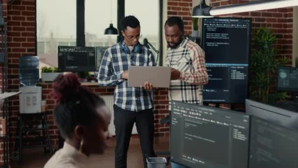 Software programmers talking about algorithms holding laptop and standing in the middle of it office — Vídeo de Stock