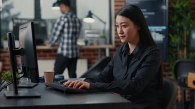 Smiling asian database software developer writing programming code on computer keyboard