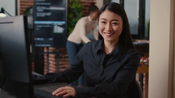 Asyalı yazılım geliştirici gülümsüyor ve bilgisayar klavyesinde yazım kodu yazmaya devam ediyor — Stok video