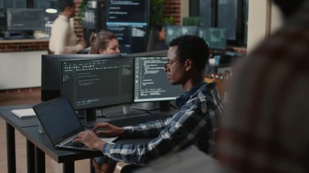 Focused programer fixing glasses while typing on laptop sitting at desk with multiple screens — Stock Video