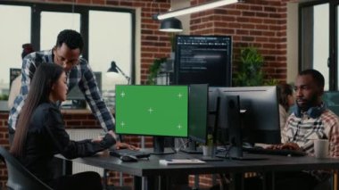 Two software developers analyzing source code looking at green screen chroma key mockup with coworker sitting at desk