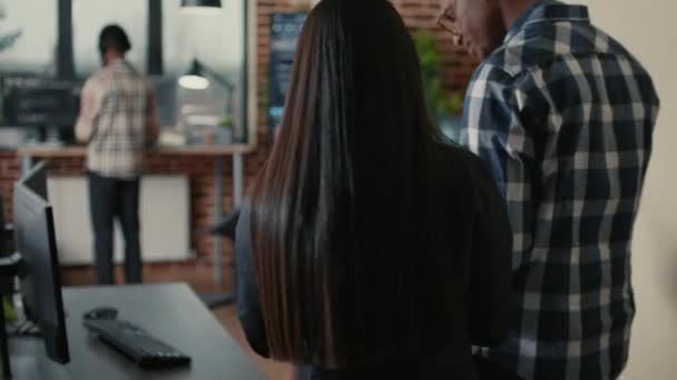 Two programers holding laptop with coding interface walking towards desk and sitting down — Video Stock