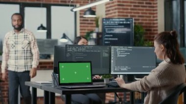 Programer working at desk with multiple computer screens and laptop with green screen chroma key mockup