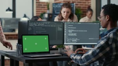 Programer taking glasses off talking with colleague at desk with laptop with green screen chroma key mockup