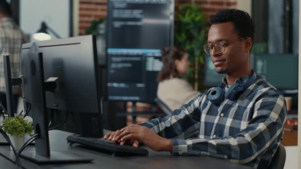 Портрет фокусованого програміста, що пише код фіксуючи окуляри і посміхаючись сидячи за столом — стокове відео