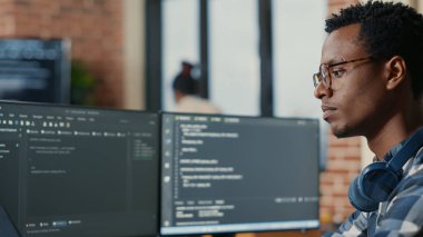 Portrait of focused software developer writing code arranging glasses sitting at desk