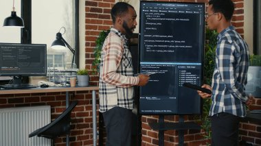 Team of software engineers leaving after analyzing source code on wall screen tv comparing errors