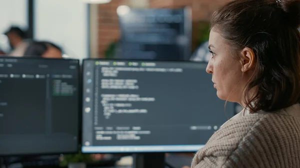 Over shoulder view of focused database designer writing code looking at multiple computer screens — Foto Stock