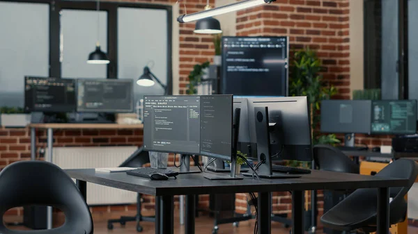 Computer screens running programming code in empty software developing agency office — Stock fotografie