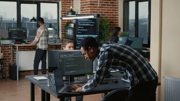 Senior developer coding on laptop at desk with computer screens parsing code — ストック写真