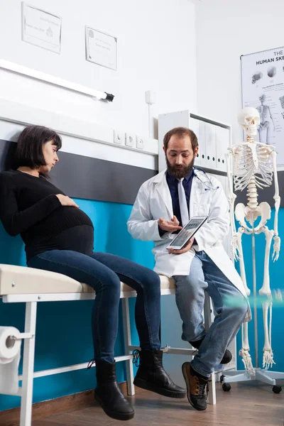 Physician explaining osteopathy scan on tablet to pregnant patient — Stok fotoğraf