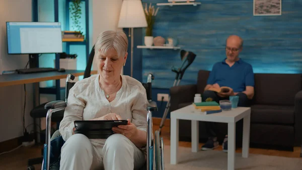 Persona in pensione che utilizza tablet digitale e seduta in sedia a rotelle — Foto Stock