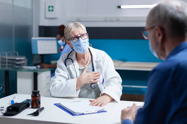 Woman doctor having checkup appointment with old patient, wearing face mask — Stockfoto