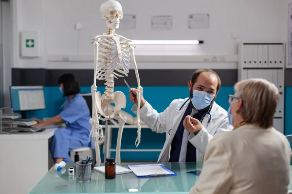 Medic explaining human skeleton to elder adult at checkup visit — 스톡 사진