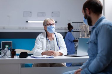 General practitioner talking to man about disease and healthcare, wearing face mask