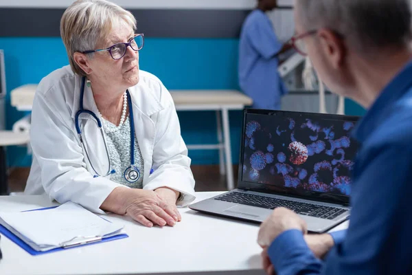 Крупним планом медик і пацієнт обговорюють ілюстрації вірусних бактерій на ноутбуці — стокове фото