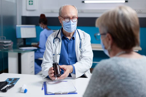 Лікар дає пляшку таблеток старшій жінці з маскою для обличчя під час медичного візиту — стокове фото