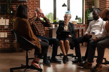 Senior person sharing depression issues with group at aa meeting, sitting in circle