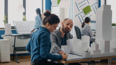 Modeli ve planlarıyla inşaat düzenini tasarlamak için takım çalışması yapan meslektaşlar