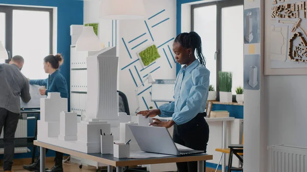 African american woman using laptop to design building model and blueprints plan. — Stockfoto